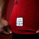 Camiseta de fútbol Umbro del Club Nacional de Football, modelo Away 2026. Diseño en color rojo con patrón de ADN en relieve, cuello en V con detalles en azul marino y blanco, y sponsors estampados en el frente y mangas. Incluye escudo del club bordado con las tres copas intercontinentales.
