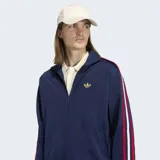 Campera deportiva Adidas Firebird azul marino con cuello alto, cierre frontal, bolsillos con cremallera y logo dorado bordado en el pecho. Presenta las tres líneas características de la marca en blanco y rojo a lo largo de las mangas.