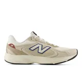Championes urbanos New Balance modelo Amaste, color beige con detalles en azul y rojo. Presentan una combinación de malla y superposiciones sintéticas, con el logo N característico en los laterales y suela de goma.