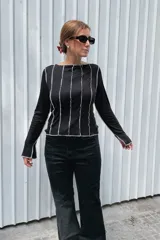 Remera de manga larga color negro, con cuello redondo y diseño de costuras verticales expuestas en color blanco que recorren el frente y las mangas.