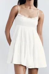 Vestido corto negro de gasa con escote recto y tirantes finos ajustables. El corpiño tiene fruncido elástico y el ruedo es escalonado con volados. Presenta un detalle de encaje a tono en el borde del escote.