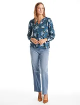Blusa de seda fría con estampado floral en tonos verdes y azules. Presenta escote en V con un aplique metálico decorativo, mangas largas con puños y corte recto.