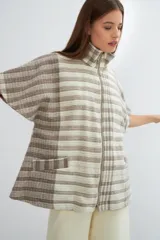 Capa acampanada color beige con manga corta, cierre metálico a la vista, cuello recto, bolsillos con tapa y terminaciones envivadas. Confeccionada en lana fina sin teñir, diseñada exclusivamente por Don Baez.