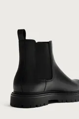 Bota Chelsea negra de estilo urbano con parte superior lisa, piezas elásticas laterales, tirador trasero y suela track con volumen.