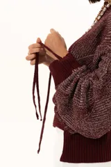 Buzo de punto color vino con diseño de trama geométrica, cuello redondo, mangas largas con puños ajustables mediante cordones y terminaciones acanaladas.