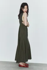 Vestido midi de tejido fluido en color verde oscuro, con cuello redondo y diseño sin mangas. Presenta un corte entallado en el torso que se abre en una falda evasé con pliegues en el bajo. Incluye cierre lateral con cremallera oculta y abertura con botón en la espalda.