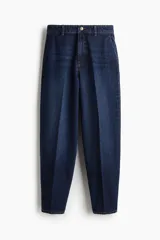 Jean tobillero de denim rígido en tono azul oscuro, con corte de tiro alto, diseño curvo y voluminoso en las piernas, y pliegues frontales y traseros.