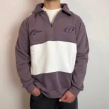 Buzo de algodón con medio cierre frontal y cuello tipo polo. Presenta un diseño de bloques de color en tonos gris oscuro y blanco, con bordados decorativos en el pecho.