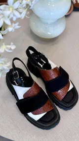 Sandalias de plataforma con suela track negra. Presentan un diseño de tiras anchas combinadas en cuero con textura de reptil color marrón y una franja central de charol negro. Incluyen una tira trasera elástica para mayor sujeción.