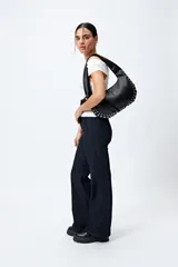 Jean negro de calce flare con cinturón incorporado en la misma tela y silueta ajustada en cadera que se ensancha hacia el ruedo.