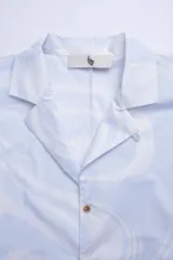 Camisa estilo camper, de fit boxy, confeccionada en popelina con estampa de mármol celeste y blanco. Tiene cuello tipo camp-collar y botones de madera.