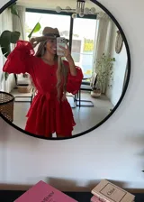 Vestido camisero corto de muselina, color negro, con mangas largas abullonadas, falda con volados en cascada y cierre frontal con botones de coco. Incluye lazo ajustable en la cintura.