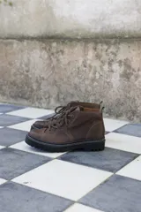 Borcegos de cuero charolado negro con cordones jaspeados en tonos marrones y suela track dentada con costura blanca visible.