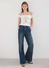 Jeans de denim azul de tiro medio, corte wide leg con diseño amplio y fluido, bolsillos delanteros y traseros, y cierre frontal con botón y cremallera.