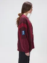 Cardigan oversize de tejido de punto grueso con diseño de bloques de color en tonos tierra. Presenta cuello en V, cierre frontal con botones, mangas largas con terminación abullonada y parches decorativos en el pecho y hombro.