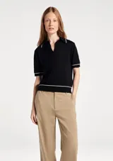 Polo de manga corta en tejido de punto color beige, con cuello tipo polo y detalles de líneas finas en color negro en el cuello, mangas y ruedo.