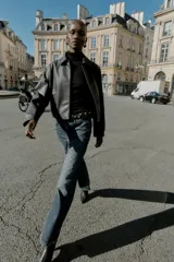 Cazadora corta negra de efecto piel, con cuello solapa, manga larga y cierre frontal con botones a presión ocultos. Incluye bolsillos delanteros de vivo con botón a presión y bajo con elástico en la espalda.