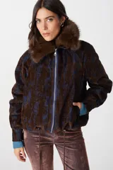 Campera de corte bomber con estampado abstracto en tonos marrón chocolate y azul. Presenta cuello de piel sintética desmontable, cierre frontal metálico, puños de tejido acanalado en color azul y cordón ajustable en el ruedo.