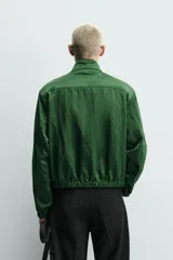 Campera verde oscuro de corte cropped y tejido técnico, con cuello alto, cierre frontal de cremallera con tirador circular, bolsillos ribeteados y puños y dobladillo elásticos.