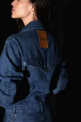 Mono largo de denim azul, con mangas largas, bolsillos delanteros y traseros, y avíos metálicos. Presenta una badana de PU en la espalda.