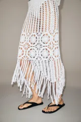 Falda midi semitransparente de punto crochet color blanco, con cintura elástica y bajo asimétrico con flecos.