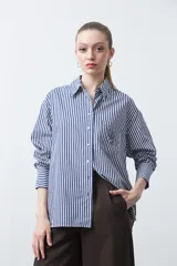 Camisa a rayas verticales azules y blancas, de manga larga con puños abotonados, cuello camisero y cierre frontal con botones. Incluye un bolsillo en el pecho con bordado de logo.