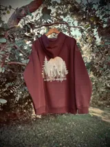 Hoodie marrón con capucha, corte oversize y estampado de paisaje montañoso en la espalda con la frase "Never Stop Exploring".
