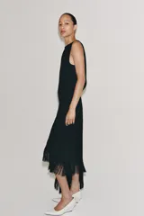Vestido midi de Zara Woman Collection color negro, sin mangas, con cuello redondo y espalda abierta. Presenta un diseño asimétrico en el bajo adornado con flecos a tono, y cierre trasero con cremallera y botón.