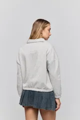 Buzo de calce relajado color tostado, con cuello alto y detalle de cordones entrelazados con ojales metálicos en el frente. Posee bolsillos laterales ocultos y puños y ruedo elastizados.