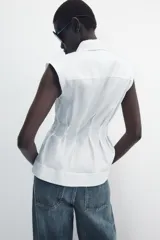 Camisa de cuello solapa y manga sisa, de color blanco. Presenta bajo acabado en peplum y cierre frontal con botones ocultos.