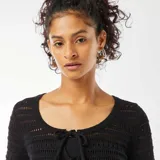 Chaqueta corta de croché color negro, con escote redondo y lazos frontales para atar.