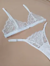 Conjunto de lencería de encaje blanco, compuesto por un soutiene de diseño triangular y una bombacha tipo colaless regulable.