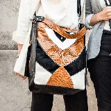 Bolso tipo morral de cuero vacuno con diseño geométrico en colores tostado, negro y blanco. Tiene manija corta y correa ajustable y removible para usar como bandolera. Cuenta con dos bolsillos verticales en los laterales. El interior está forrado y tiene un bolsillo con cierre y otro pequeño para el celular.