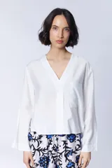 Camisa blanca de manga larga con cuello en V, cierre frontal de botones y un bolsillo de parche en el pecho.