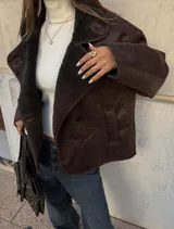 Chaqueta de gamuza marrón con interior de corderito sintético, diseño cruzado con botones y bolsillos laterales.