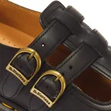 Zapatos Mary Jane Dr. Martens modelo 8065 Black Smooth, fabricados en cuero negro con doble tira ajustable mediante hebillas metálicas doradas, puntera con perforaciones decorativas tipo brogue y suela acolchada con costuras amarillas.