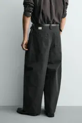 Pantalón de corte relajado confeccionado en tejido de algodón. Presenta cintura con trabillas laterales ajustables, bolsillos frontales y traseros, y un diseño distintivo de costuras laterales giradas que recorren la pernera.