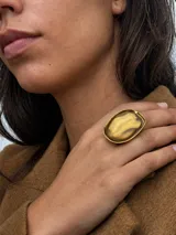 Anillo de diseño llamativo con base dorada y piedra central de resina en tono verde oliva con acabado traslúcido.