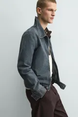 Cazadora cropped fit de denim de algodón, color negro lavado. Presenta cuello solapa, manga larga con puños abotonados, cierre frontal de cremallera y bolsillo superior con cierre de cremallera en el pecho.