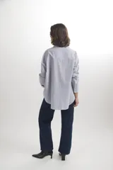 Camisa de corte oversize en color azul claro, confeccionada en algodón. Presenta cuello clásico, cierre frontal con botones, mangas largas con puños abotonados y un bolsillo aplicado en el pecho.