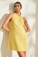Vestido corto de lino italiano, sin mangas y con cuello redondo a la base. Presenta detalles desflecados en el cuello y costura central vertical.