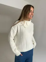 Jersey de punto color crudo con cuello alto y diseño acanalado vertical. Presenta un corte holgado y mangas largas con puños ajustados.