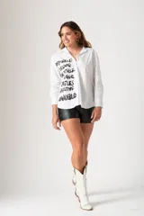 Camisa blanca de algodón con cuello clásico, mangas largas y estampado de texto en negro en el frente.