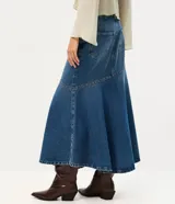Pollera midi de jean azul, de tiro medio con pretina y pasacintos. Presenta un recorte diagonal en la parte inferior decorado con pequeñas tachas metálicas.