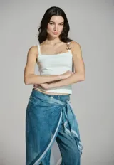 Musculosa blanca de líneas sencillas, con escote cuadrado y tirantes finos que presentan un detalle de ancla dorada en uno de ellos.