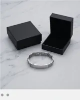 Pulsera rígida de acero inoxidable con diseño de guarda griega en los extremos y placa central lisa apta para grabado.