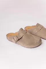 Zueco de acabado cuero gamuzado color beige, con diseño cerrado y tira con hebilla metálica regulable en el empeine. Posee plantilla anatómica y suela con textura.