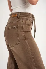 Pantalón jean de corte barrel y tiro alto, en tono marrón lavado, con bolsillos laterales y traseros, y lazo ajustable en la cintura.