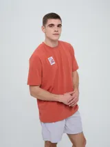 Remera de manga corta color beige, con cuello redondo y diseño holgado. Cuenta con un pequeño estampado rectangular en el pecho con motivo futbolero.