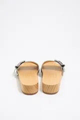 Sandalias de madera con tira ancha de cuero sintético negro con textura de cocodrilo, hebilla metálica plateada y apliques de tachas plateadas.